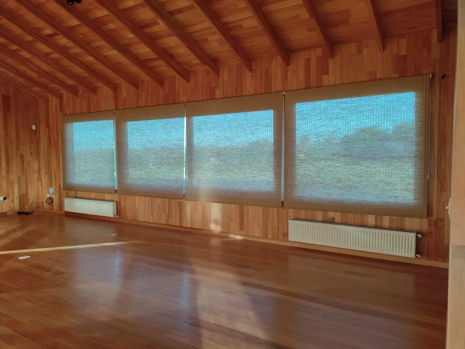 Cortinas roller screen en una fila de ventanas de una sala con paredes de madera